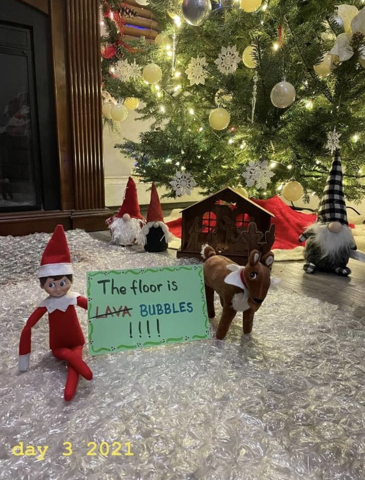 an elf with a sign in front of a christmas tree that says the floor is lava bubbles