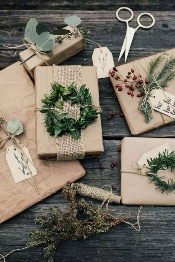 presents wrapped in brown paper, tied with twine and decorated with greenery are sitting on a wooden table