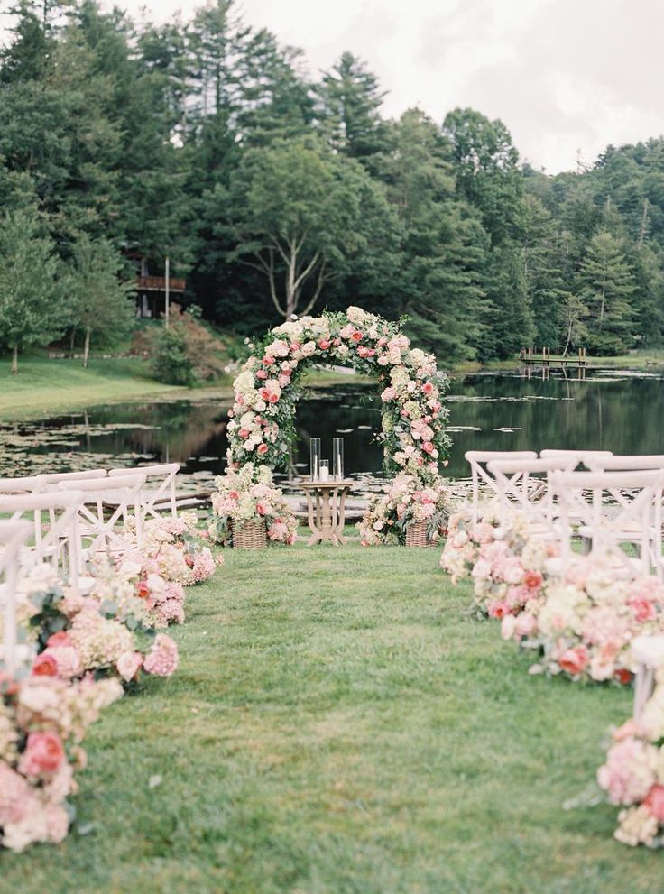 an outdoor wedding ceremony setup with white chairs and pink flowers on the aisle, surrounded by greenery