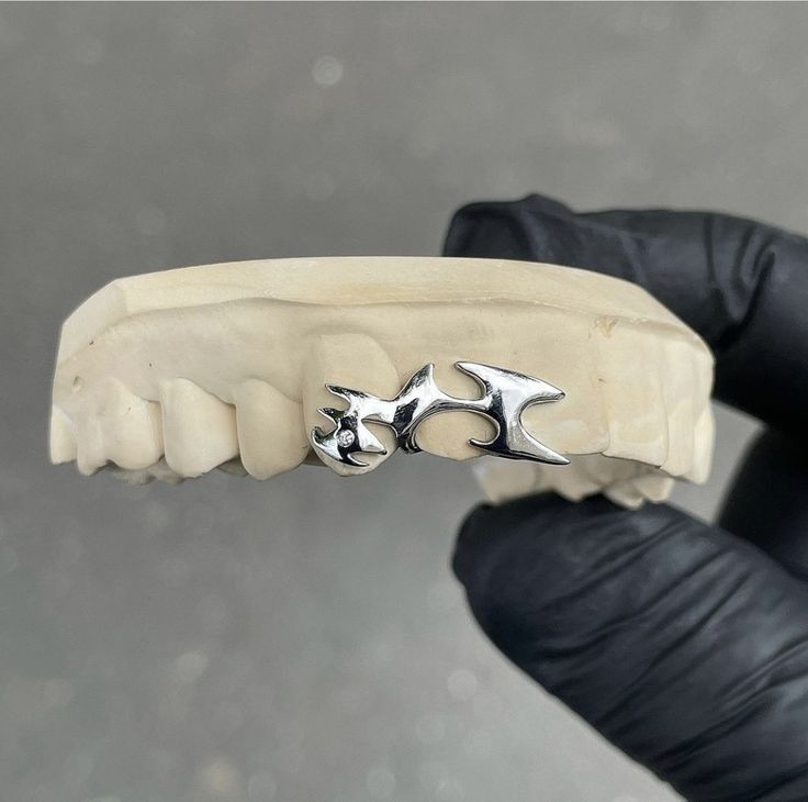 a person wearing black gloves and holding a fake tooth with two silver teeth on it