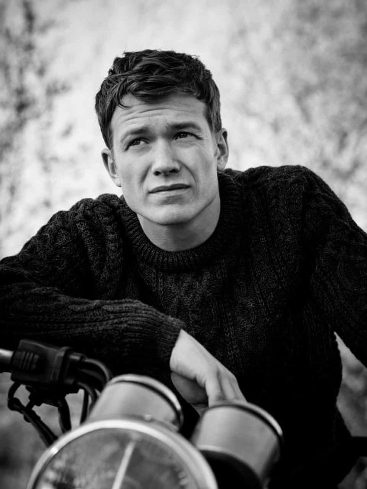 a black and white photo of a man sitting on a motorcycle with his hand on the handlebars