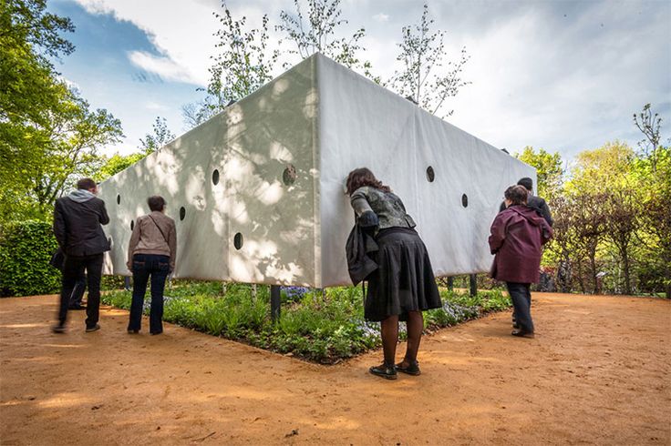 several people standing around a white structure in the middle of a dirt area with trees and bushes