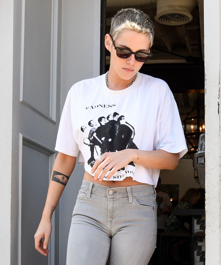 a woman with grey hair and sunglasses is walking out of a door wearing gray jeans