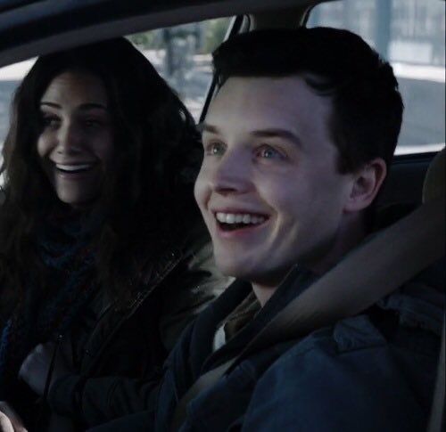 two people sitting in the back seat of a car, one smiling at the camera