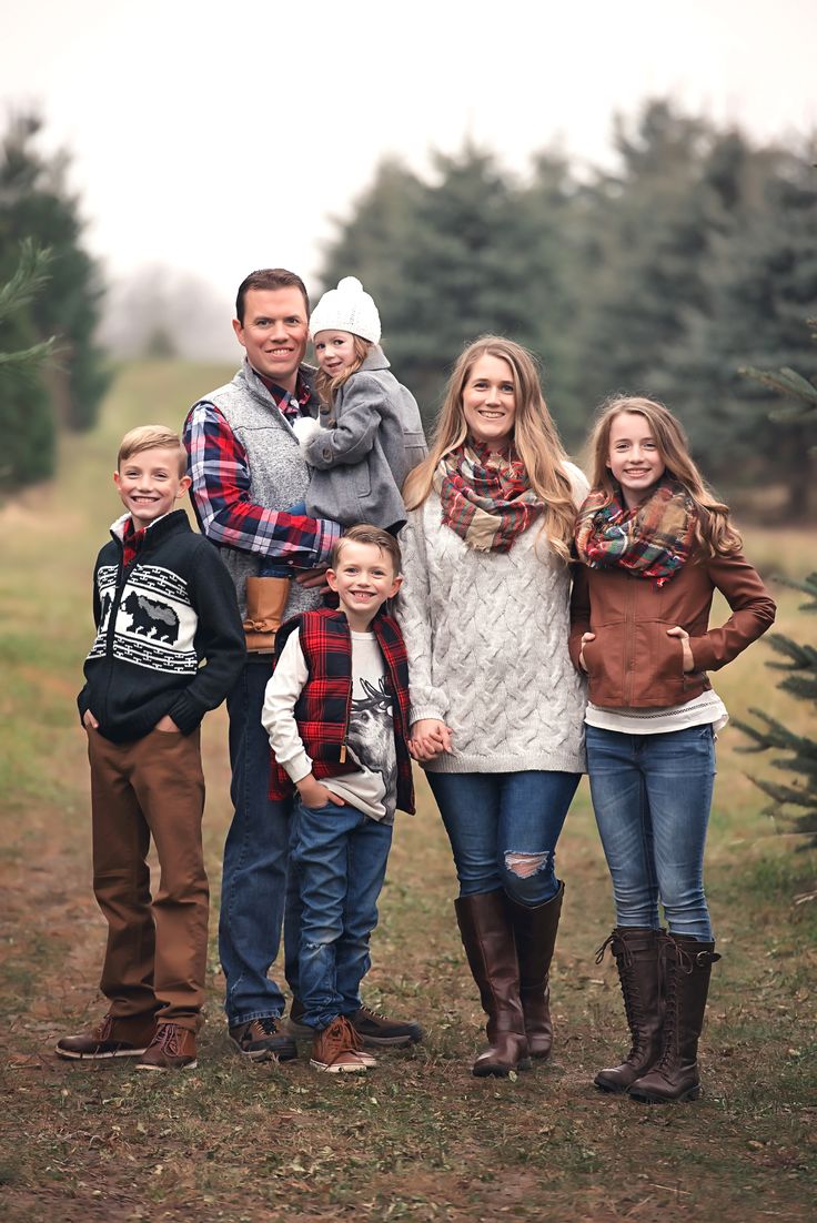 a family poses for a photo in front of a christmas tree at the farm with their two children