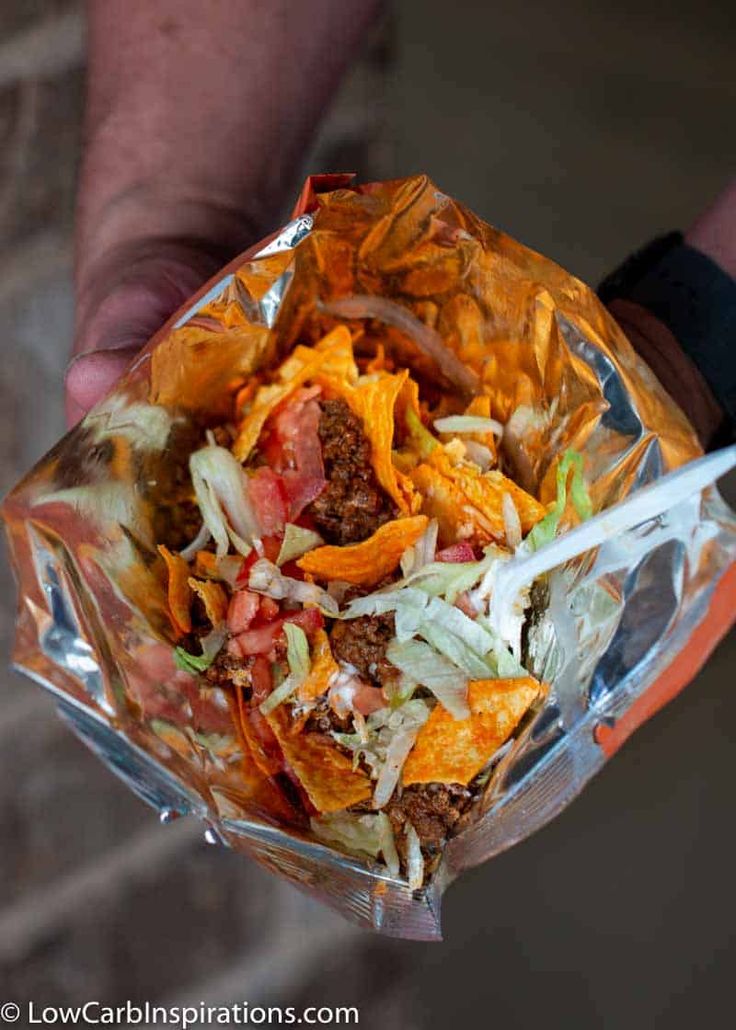 a person holding up a container filled with taco meat and lettuce wrapped in foil