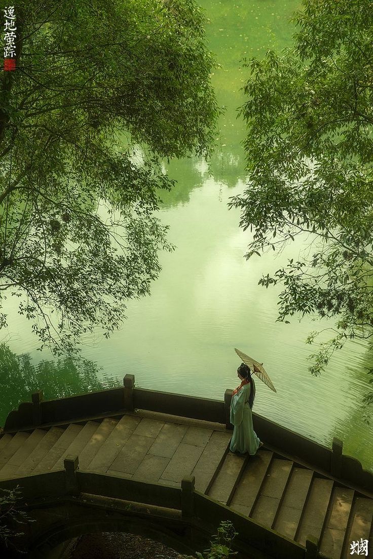 a woman sitting on top of a wooden bridge holding an umbrella