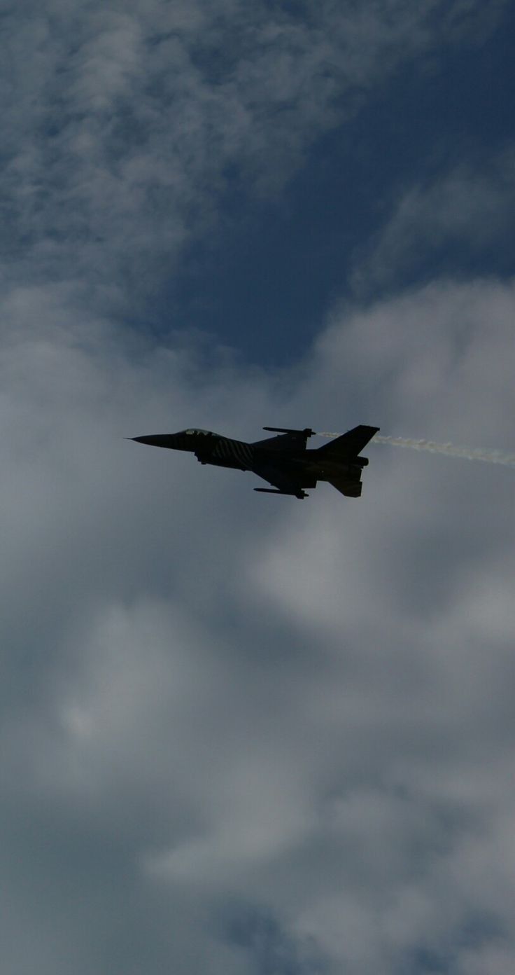 a fighter jet flying through a cloudy blue sky