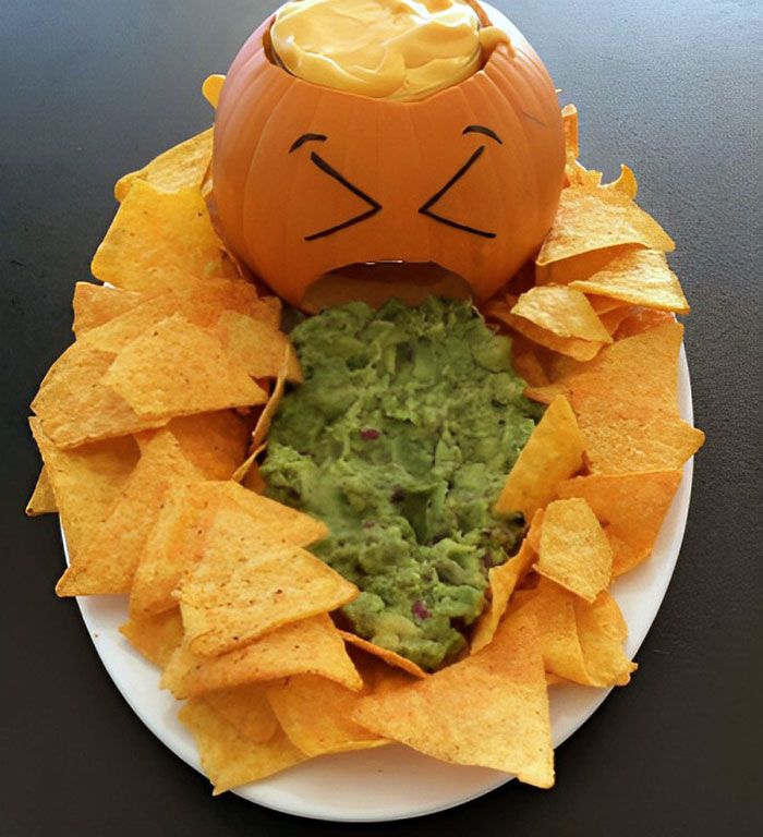 a white plate topped with chips and guacamole next to a jack - o'- lantern