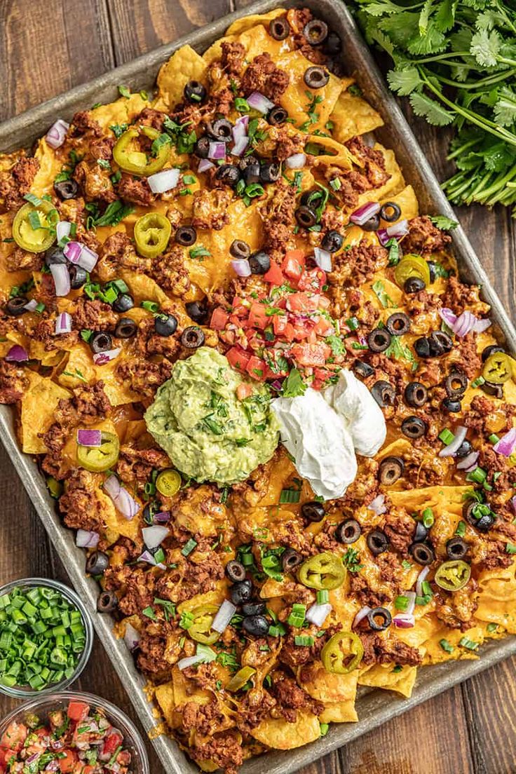 a tray filled with taco casserole and toppings on top of a wooden table