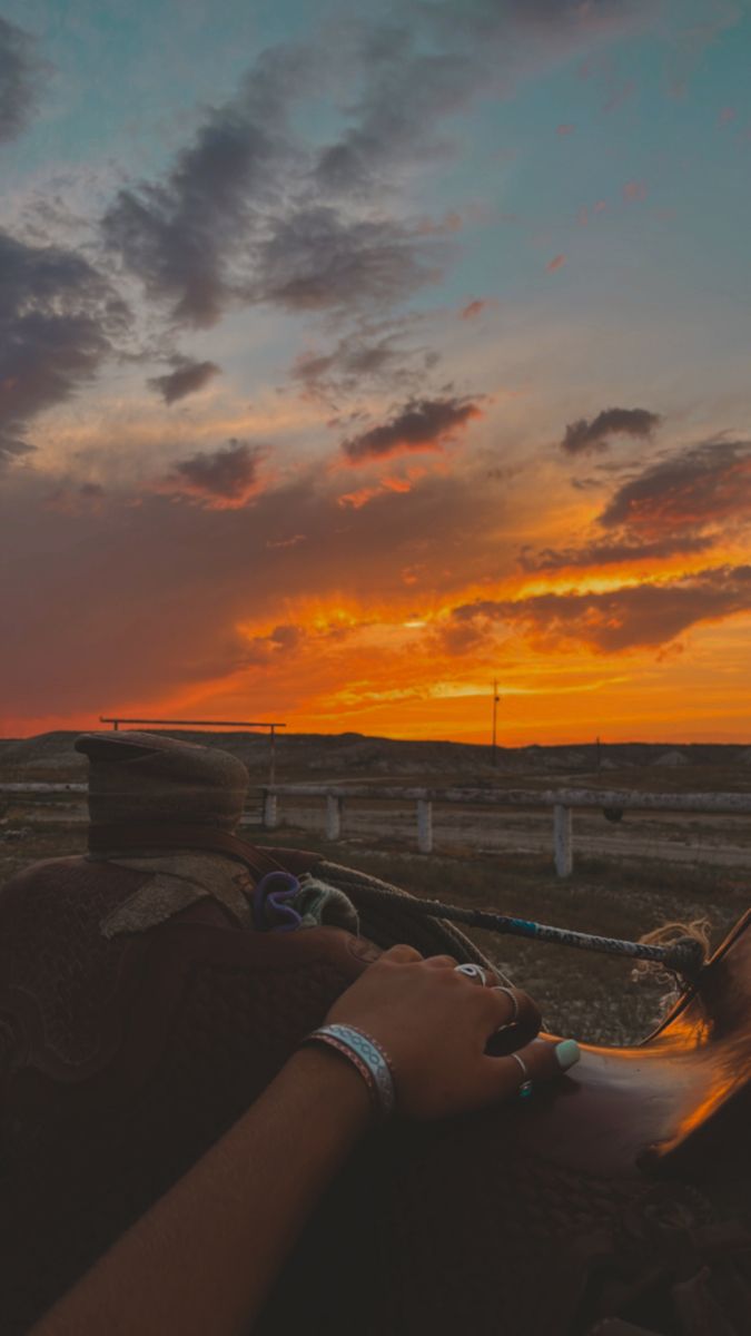 two people are sitting on a bench watching the sun go down in the distance with their arms wrapped around each other