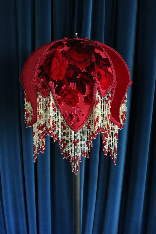 a red and gold table lamp sitting on top of a blue curtain