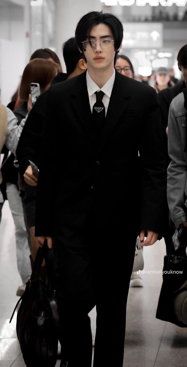 a man in a suit and tie walking down a hall way with other people behind him