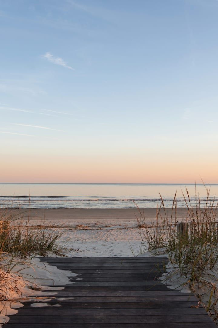 a wooden walkway leading to the beach at sunset with sea oats in the foreground