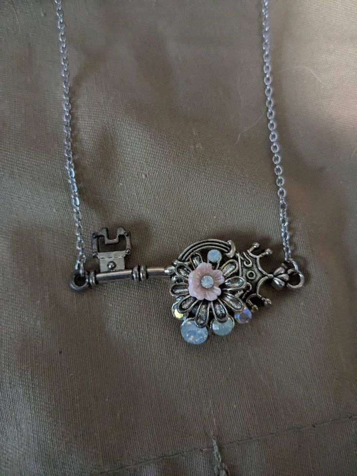 Flowers and opal stones adorn this crown key. Metal Key Pendant Jewelry, Key Pendant Jewelry In Metal, Metal Jewelry With Keys For Gifts, Key Detail Metal Jewelry As A Gift, Silver Key Pendant Jewelry, Vintage Metal Jewelry With Keys Detail, Vintage Metal Jewelry With Keys, Vintage Metal Jewelry With Two Keys, Vintage Pendant Jewelry With Keys