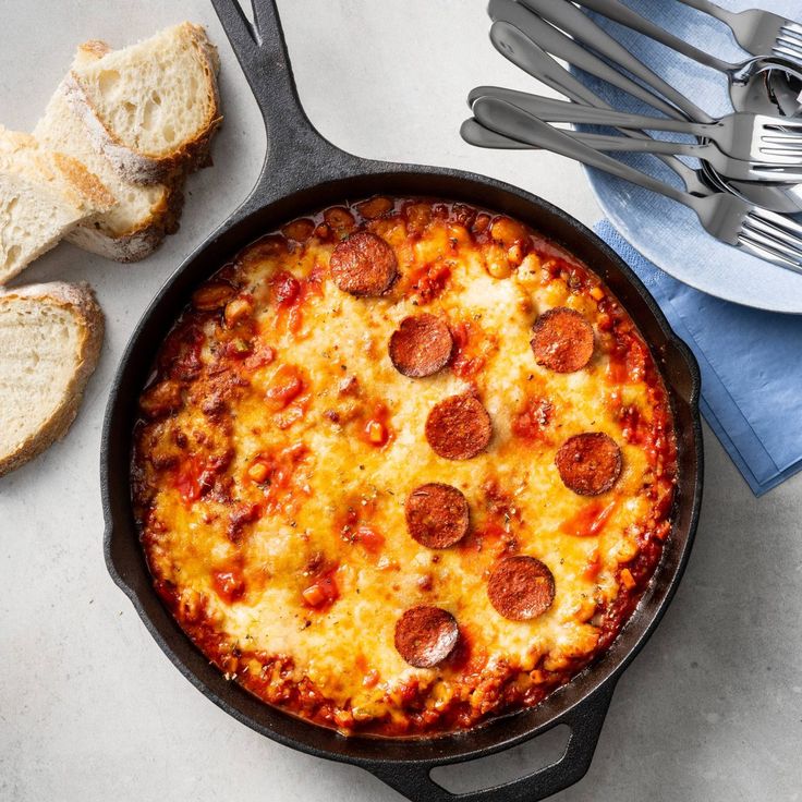 a pepperoni pizza in a cast iron skillet with slices of bread on the side