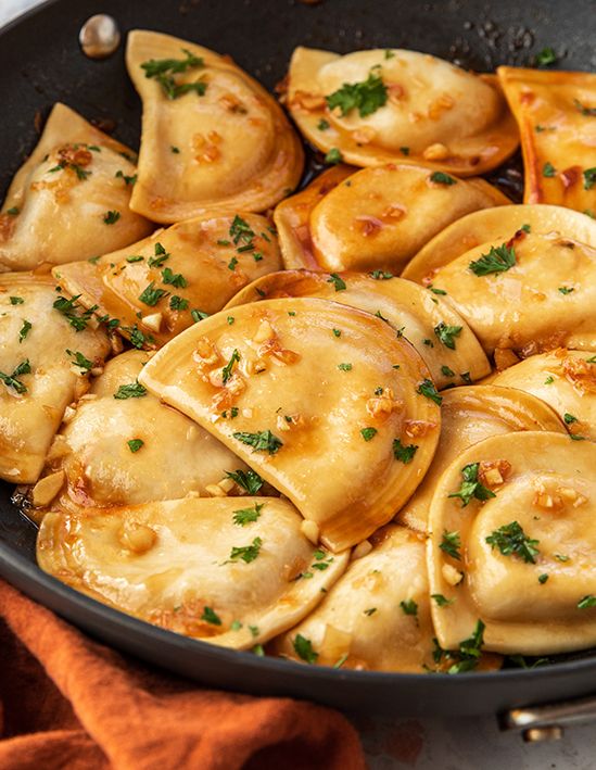 a skillet filled with dumplings covered in sauce and parsley on the side