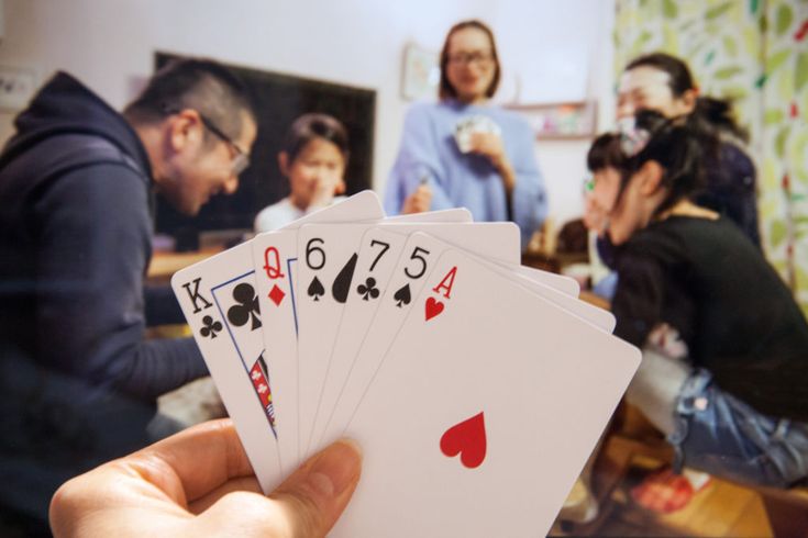 a hand holding four playing cards in front of a group of people sitting at a table