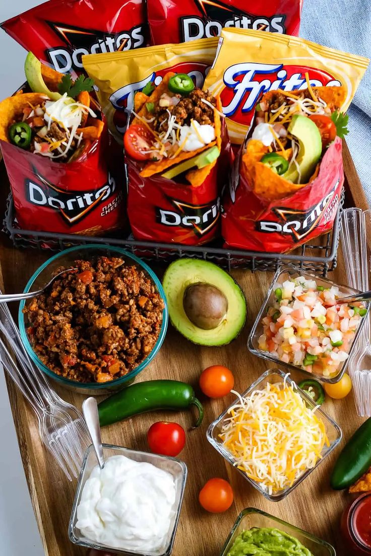 mexican food is laid out on a cutting board, including tortilla chips, salsa, guacamole, and sour cream cheese