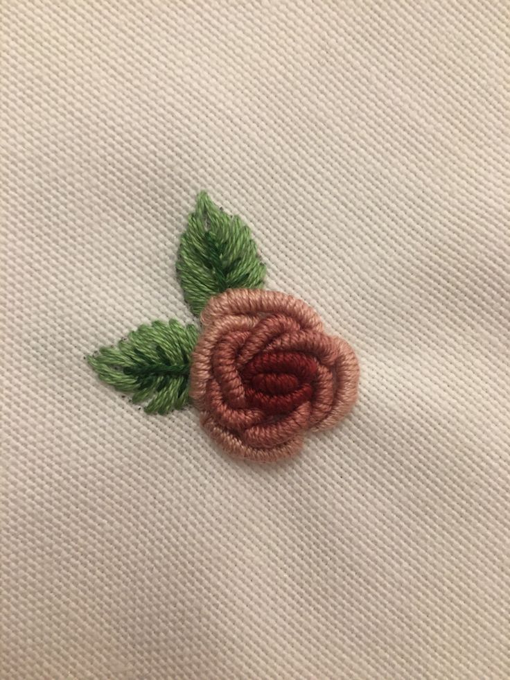 a close up of a rose on a white cloth with green leaves and thread in the middle