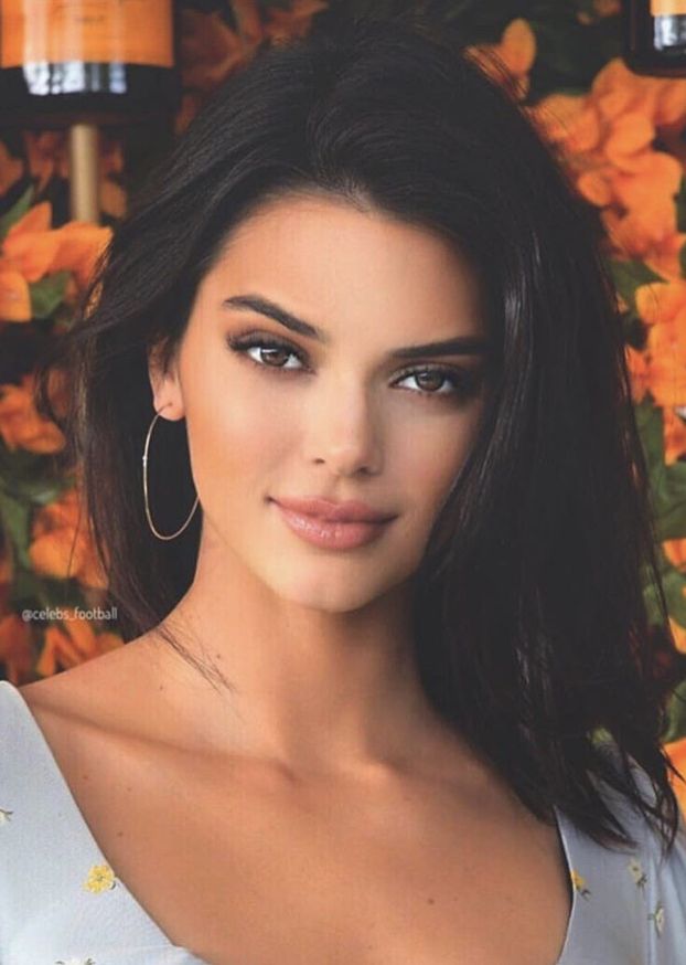 a close up of a person wearing large hoop earrings and a white top with yellow flowers in the background