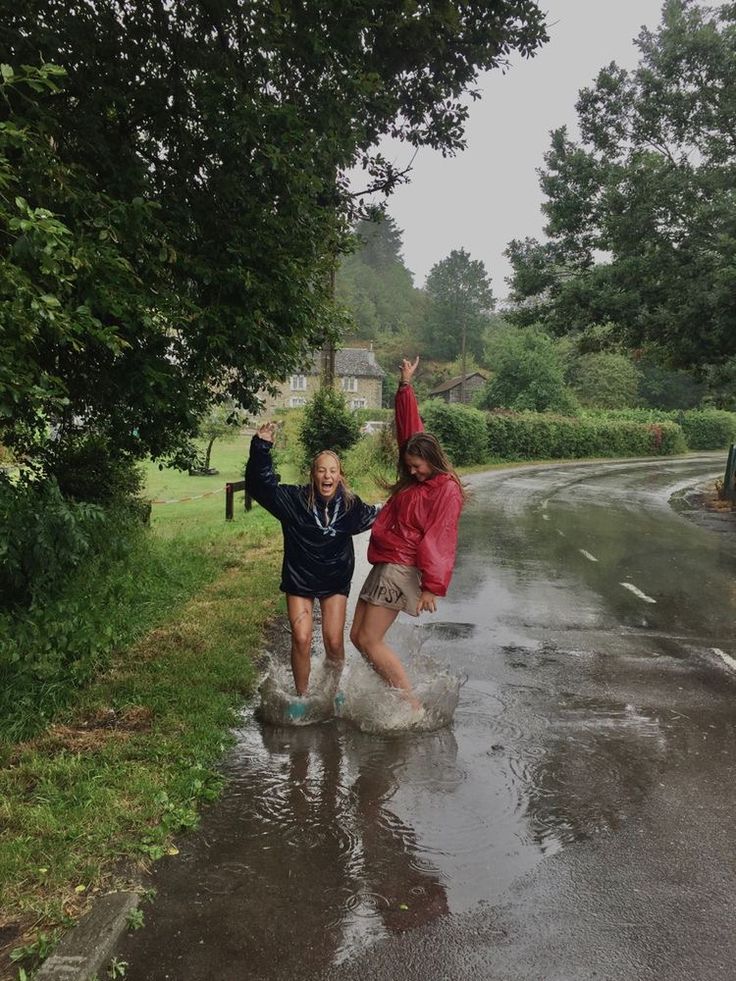 two girls are playing in the rain with an umbrella