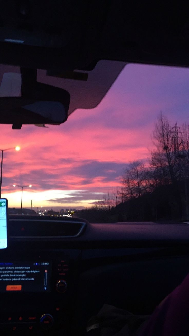 the sun is setting in the distance as seen from inside a car with dashboard lights on