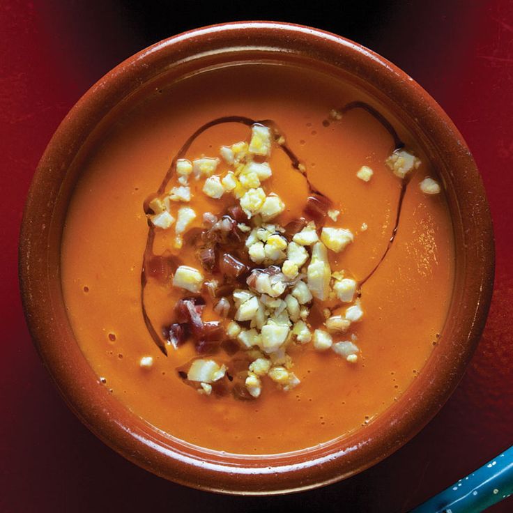 an orange bowl filled with food on top of a red table next to a blue spoon