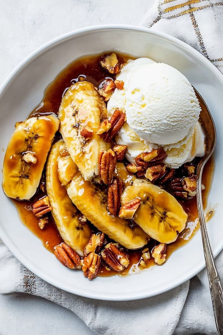 a white plate topped with bananas and pecans next to ice cream on top of a table