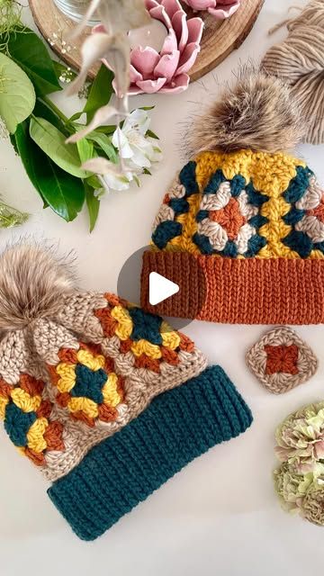 two knitted hats with pom poms on top of them next to flowers