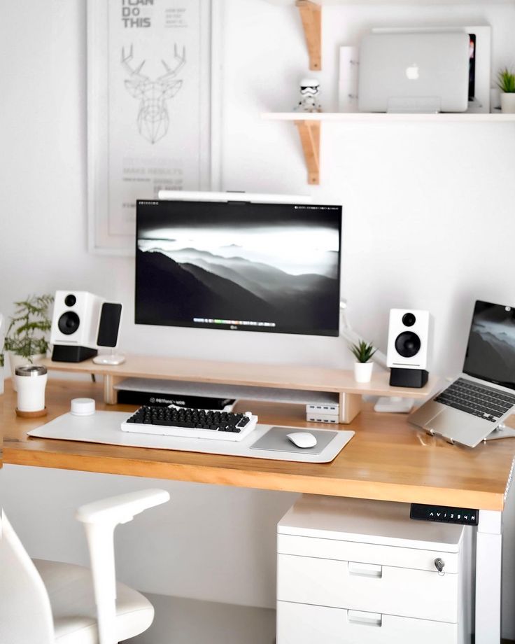 a desk with a computer, laptop and speakers on it in front of a white wall