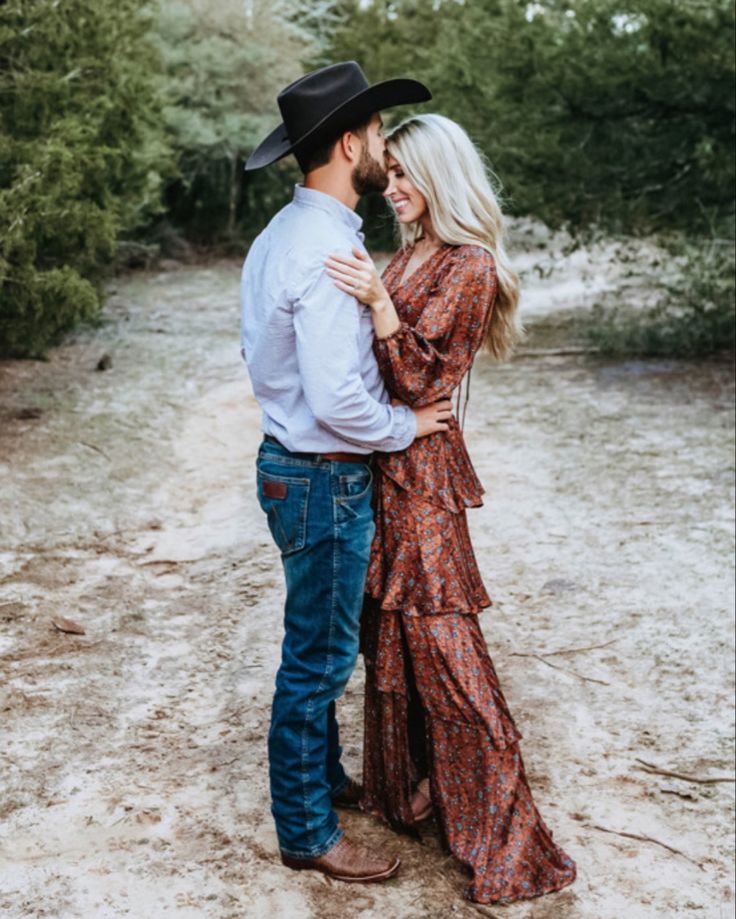 a man and woman in cowboy hats standing together on a dirt road with trees behind them