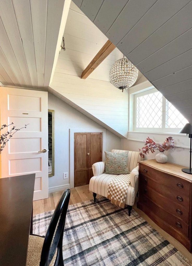 an attic bedroom with white walls and wood flooring, a chair in the foreground