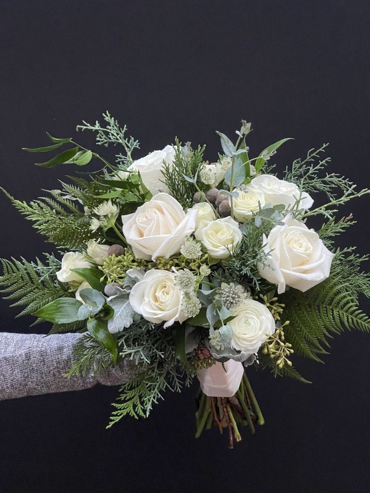 a bouquet of white roses and greenery in someone's hand