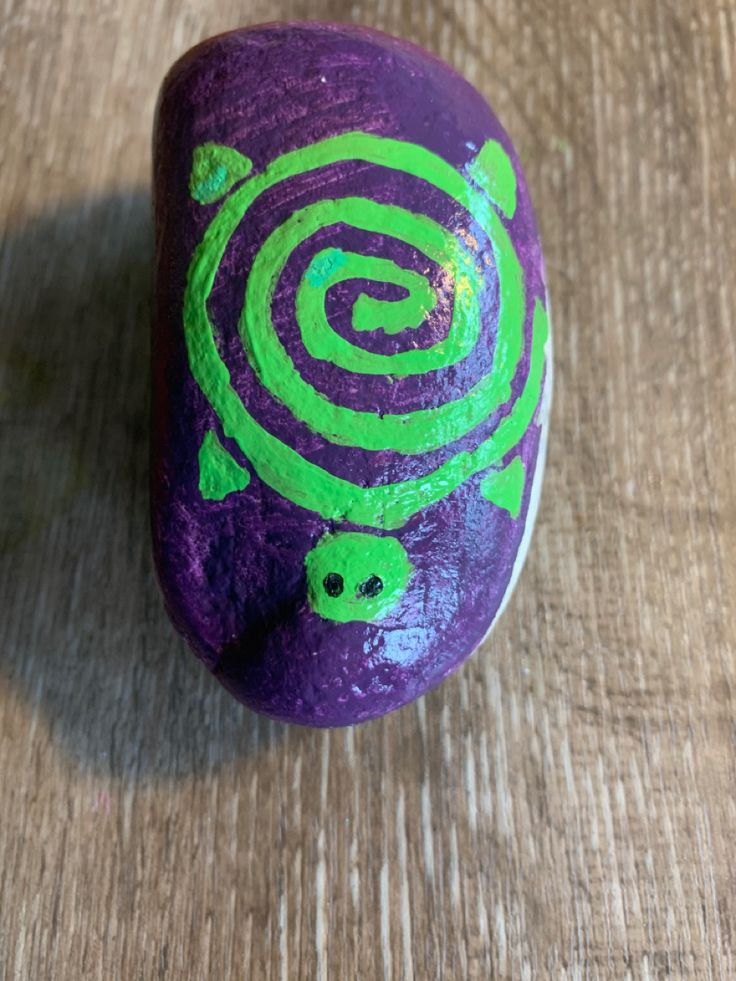 a purple and green painted rock sitting on top of a wooden table