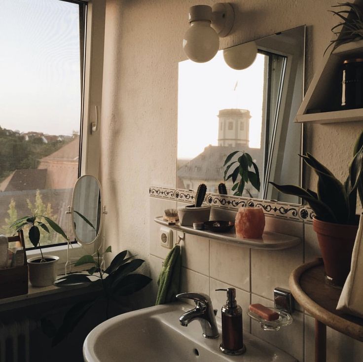 a bathroom sink sitting under a window next to a white counter top with potted plants on it