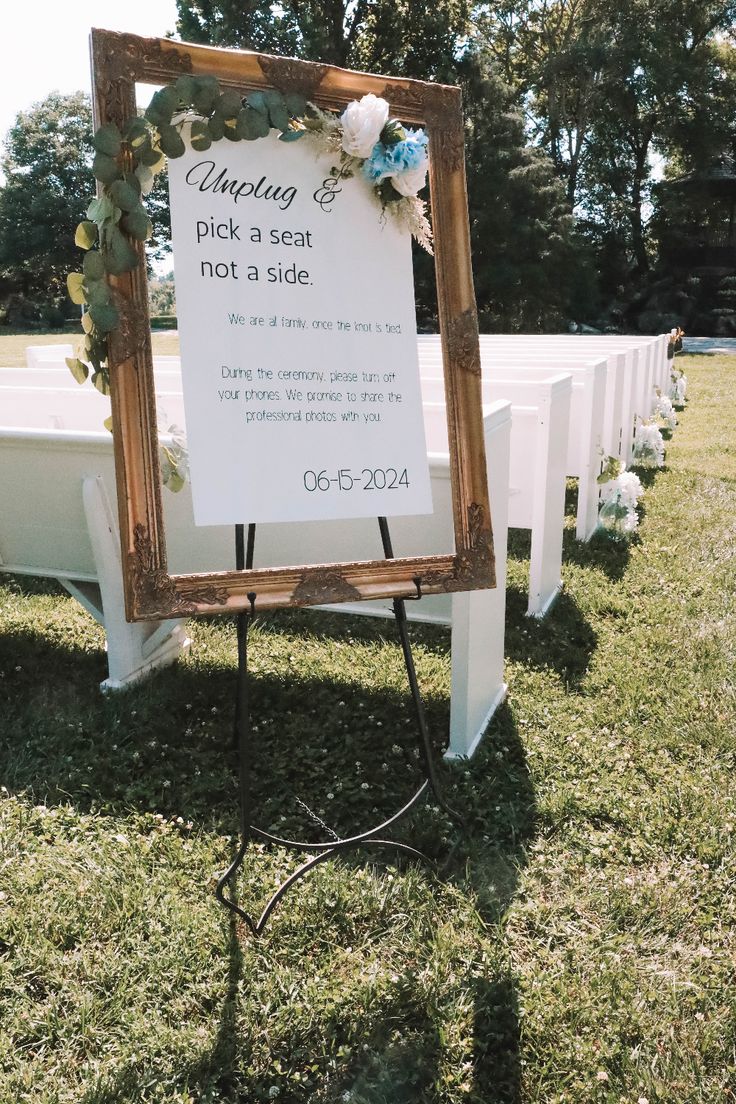 a sign that is sitting in the grass near some white benches with flowers on it