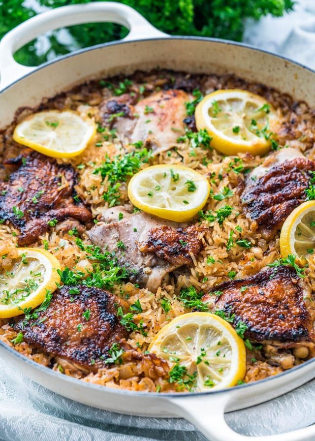 a pan filled with rice and lemons on top of a table next to parsley