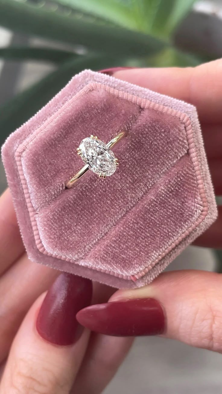 a woman's hand holding a pink velvet ring box with a diamond in it