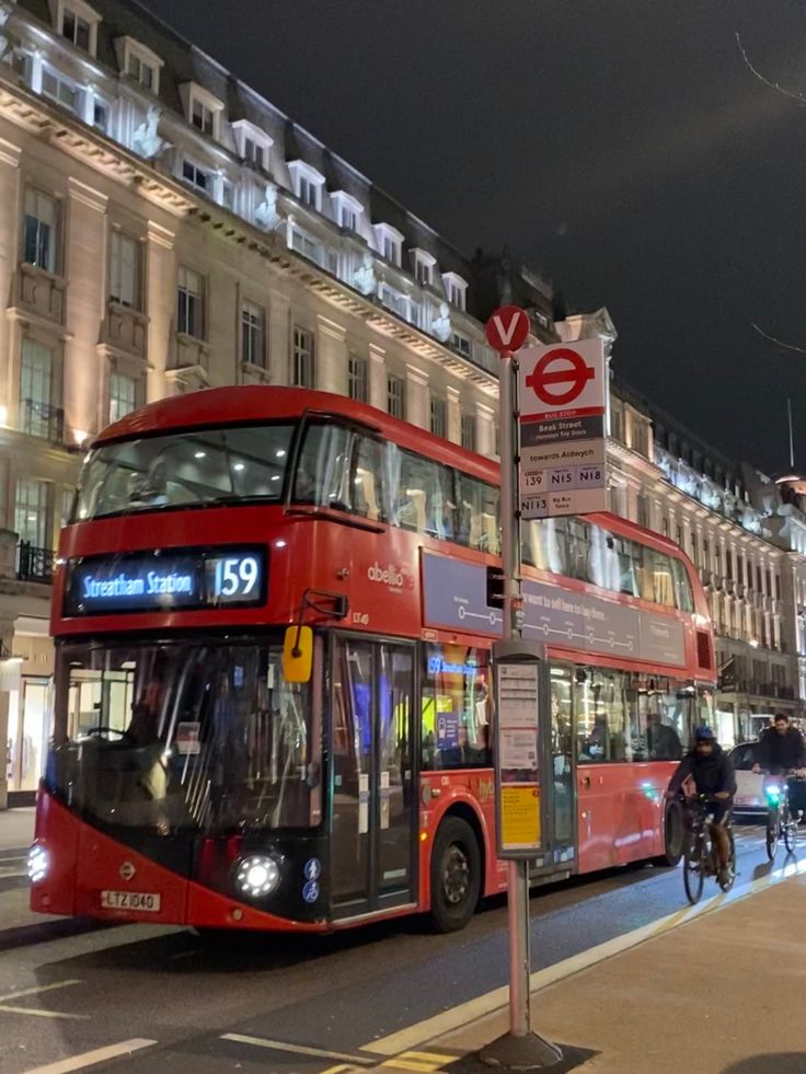 a red double decker bus driving down a street next to tall buildings and traffic lights