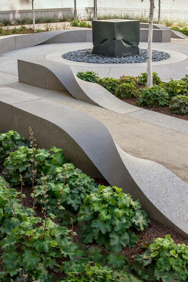 an outdoor area with plants, rocks and a sculpture in the center surrounded by shrubbery