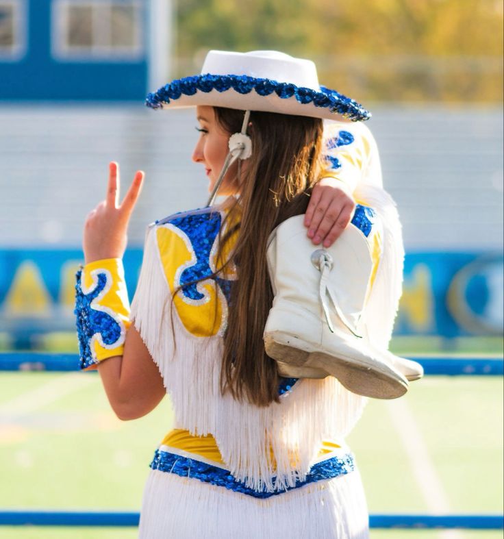 a woman wearing a white and blue outfit with a hat on her head holding a shoe