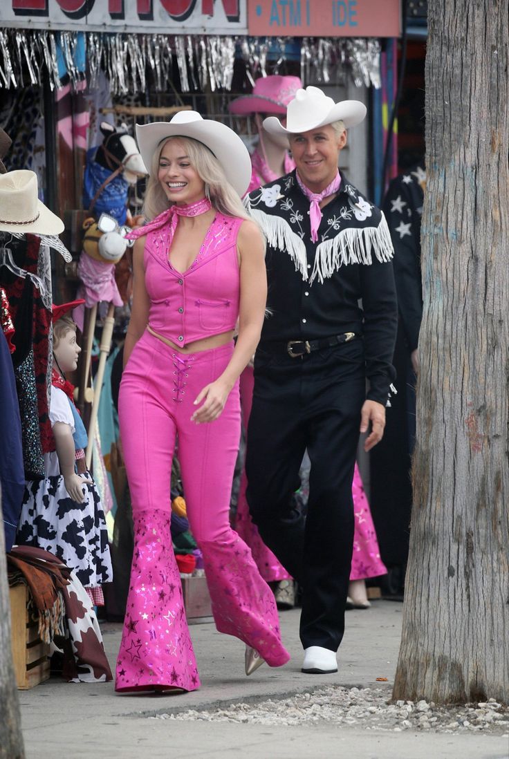 two women in pink outfits are walking down the street with cowboy hats on their heads