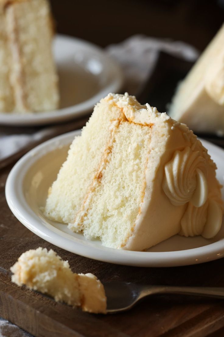 a slice of white cake on a plate with a fork next to it and another piece in the background