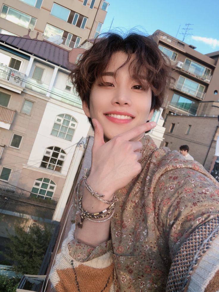 a woman with short hair and bracelets posing for a photo in front of some buildings