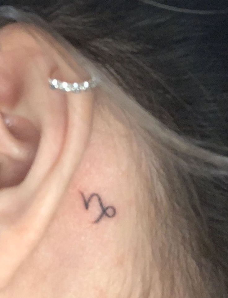 a woman's ear with a small zodiac sign tattoo on it