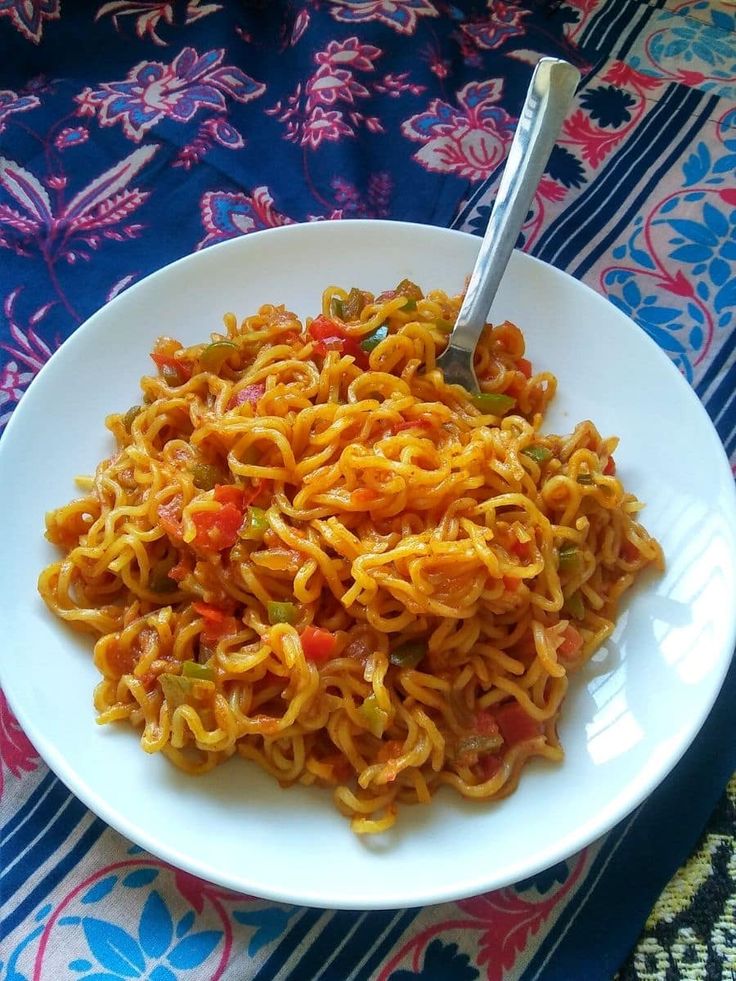 a white plate topped with noodles and vegetables on top of a blue table cloth next to a fork