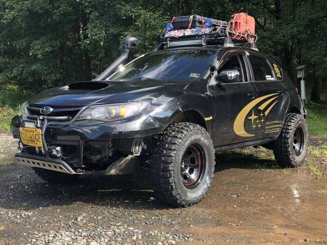 a black four door suv parked on top of a dirt road in front of trees