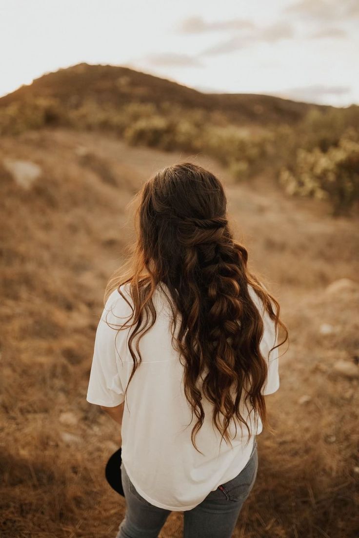 a woman with long hair standing on a hill looking down at the ground and grass