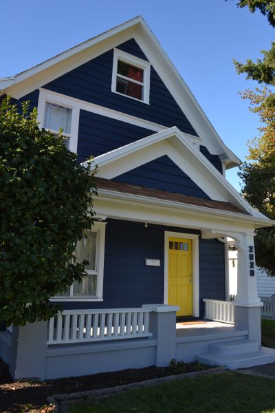 a blue and white house with a yellow door on the front porch is seen in this image